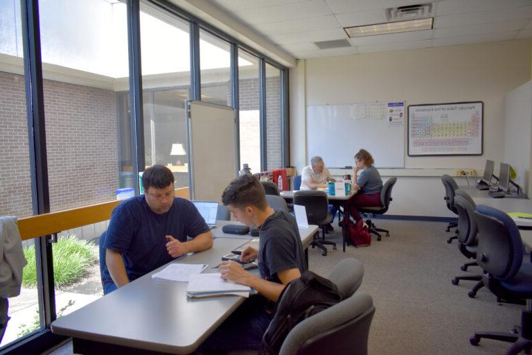 Image shows two tutors sitting and working with two students in the Tutoring Center.